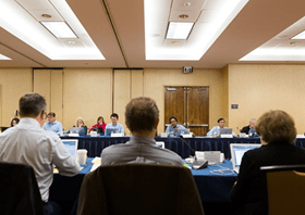 Panel of reviewers with laptops in a conference room.